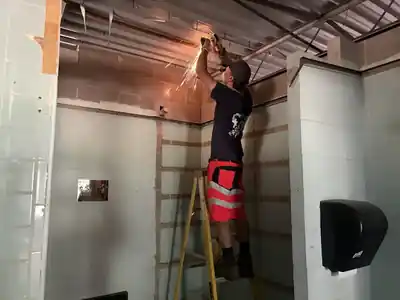 A volunteer on a ladder grinding metal in a tiled room, sparks falling
