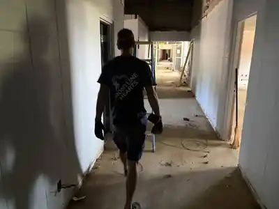A volunteer walking a dusty hallway with hanging wires and a ladder
