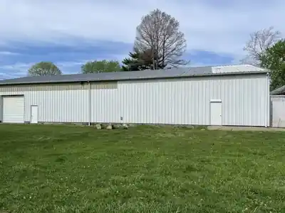 White corrugated metal shop building with roll-up door on a grassy lot